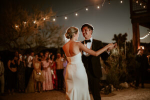 wedding couple dancing on an outdoor dance floor with lights and their guests around
