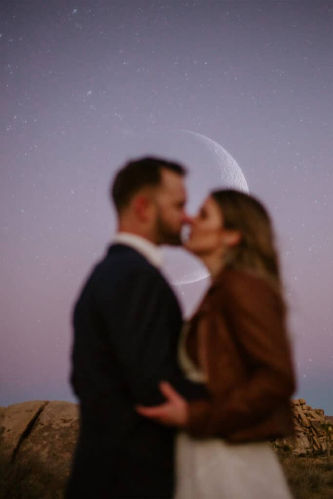 groom and bride kissing at sunset with the moon in the background