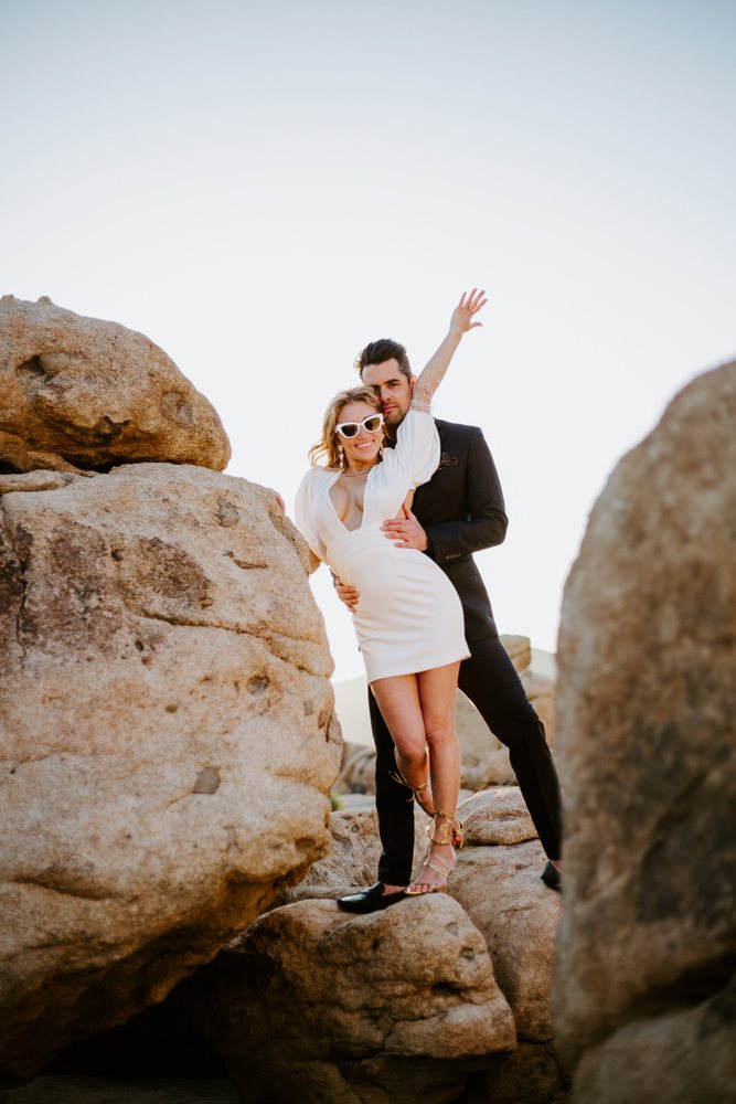 Arm raised, posing on the boulders in sunglasses