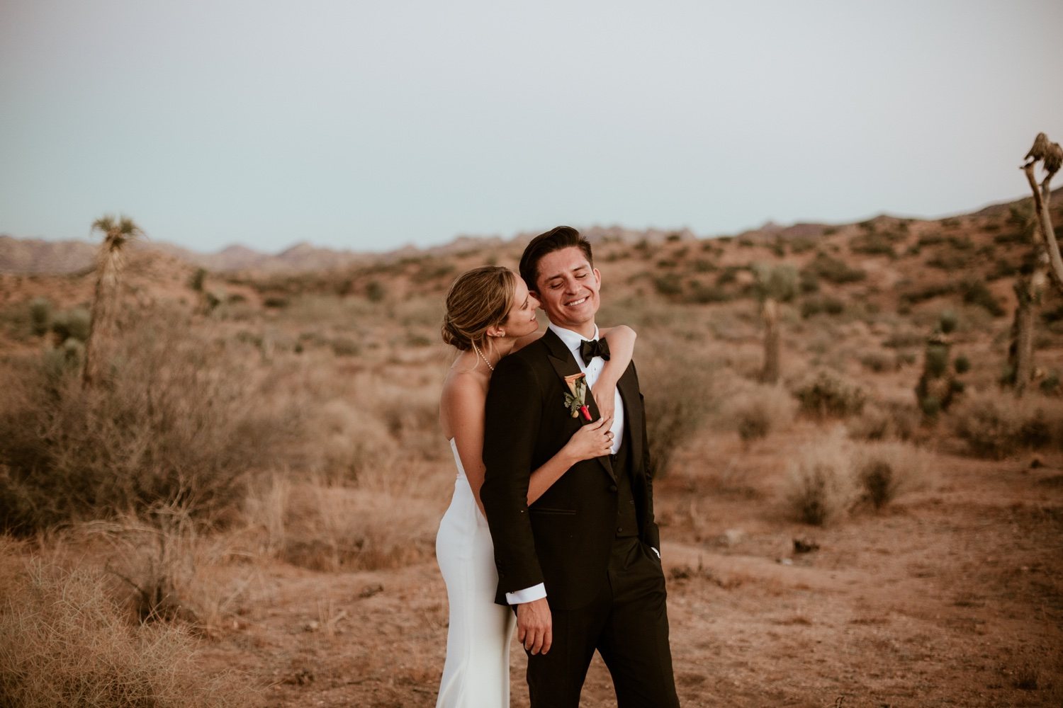 Bride hugging her groom from behind in the desert