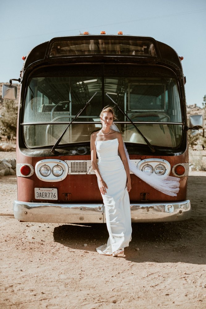Bride leaning on a vintage bus in the desert