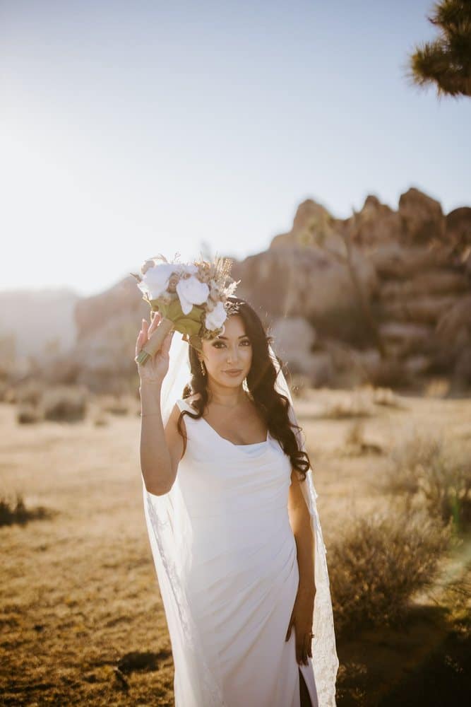 Bride raising her bouquet in the desert sun
