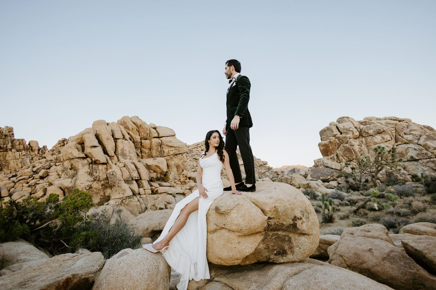 Bride sitting on a boulder, groom standing above