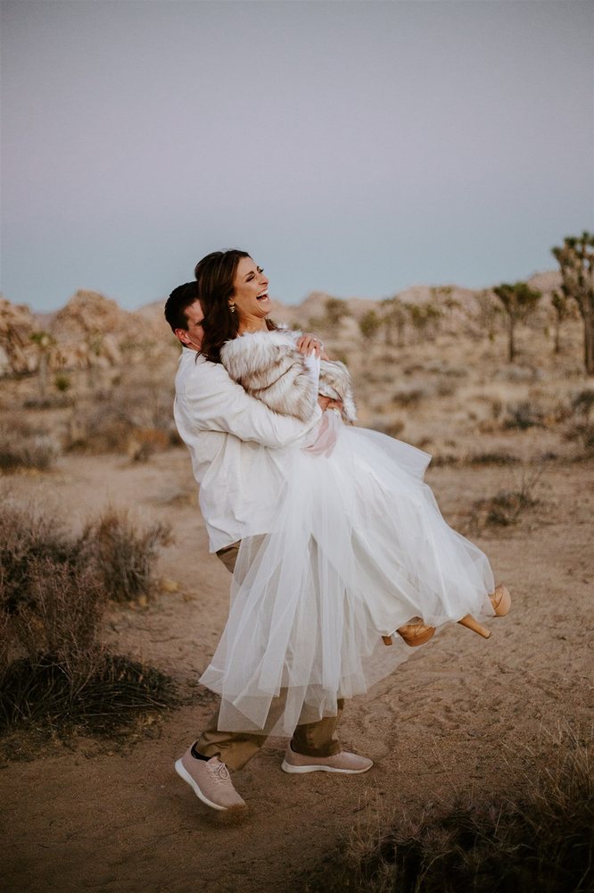 Groom lifting his laughing bride in the desert