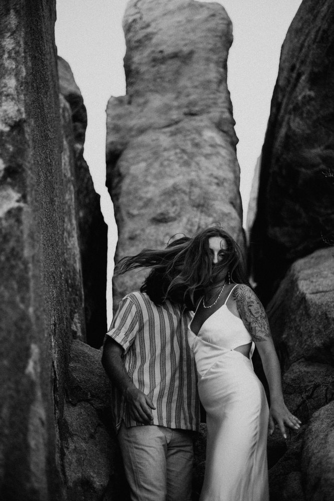 Wind-swept couple between rock towers, black and white